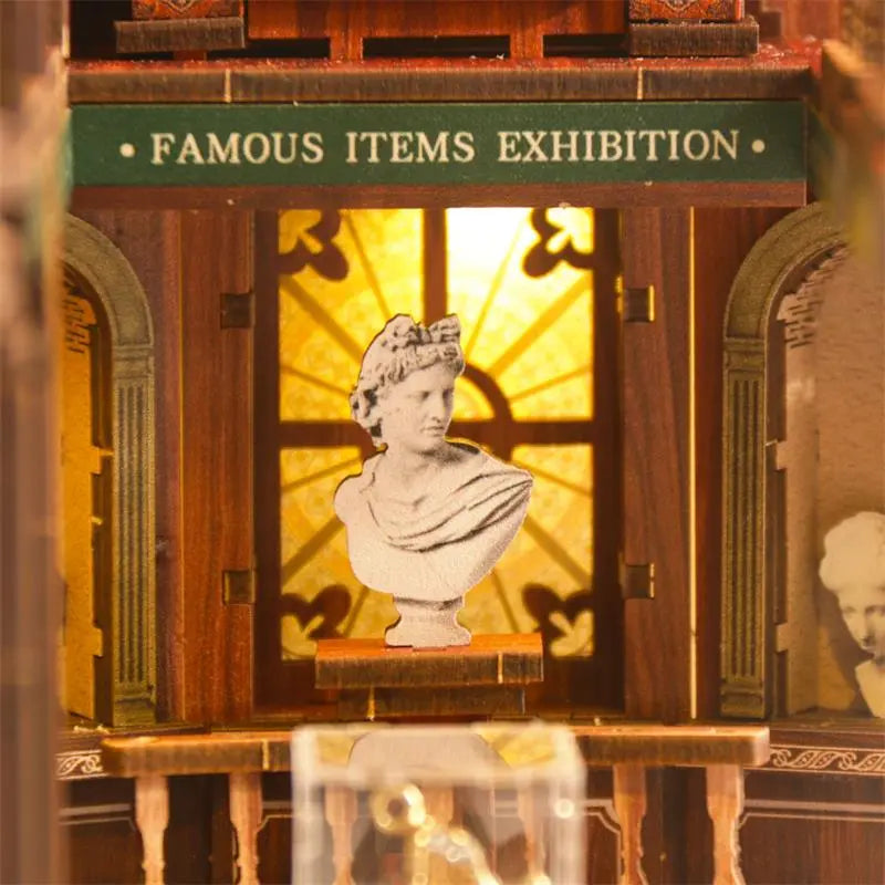 Miniature glass display case in center of first floor inside【The Philosophica Library】， clear acrylic enclosed on four sides, housing three plaster sculptures： Socrates bust on left, Venus de Milo in center, Homer bust on right, each approximately 2cm tall, with matte granular texture simulating plaster