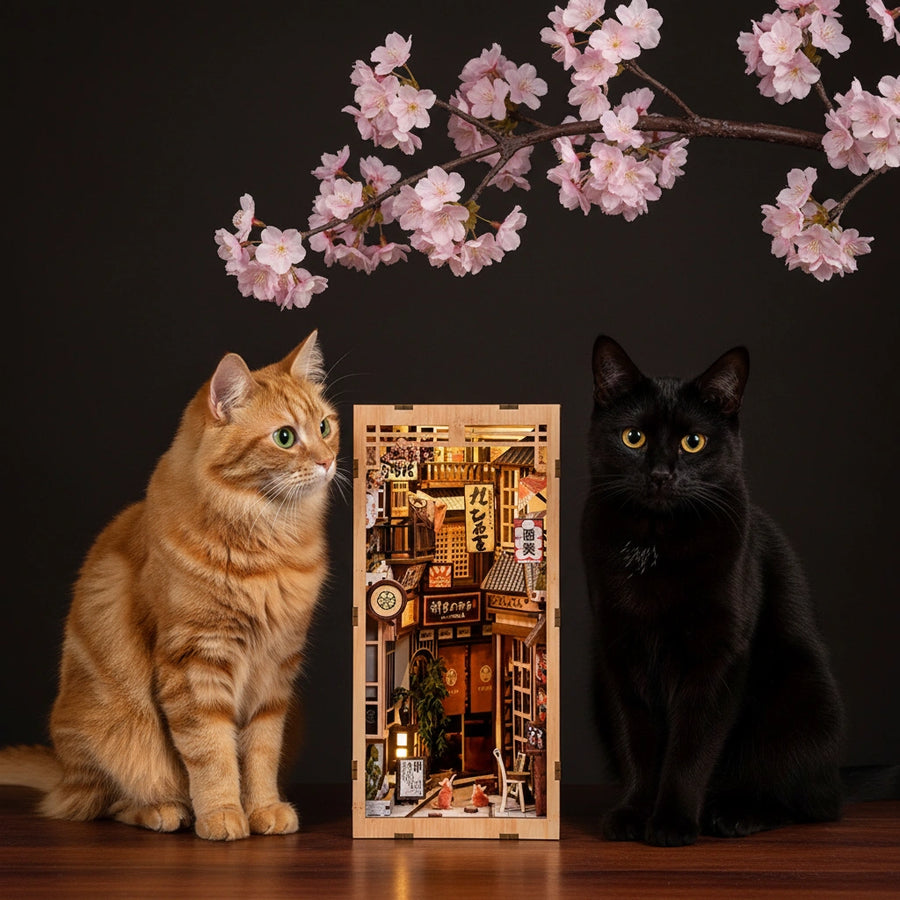 The Alley Waiting for the Cat DIY book nook miniature – white fluffy cat sitting beside Japanese alley wooden diorama with paw touching the facade, warm amber LED light glowing inside, cherry blossom petals, cozy Japanese miniature alley book nook kit
